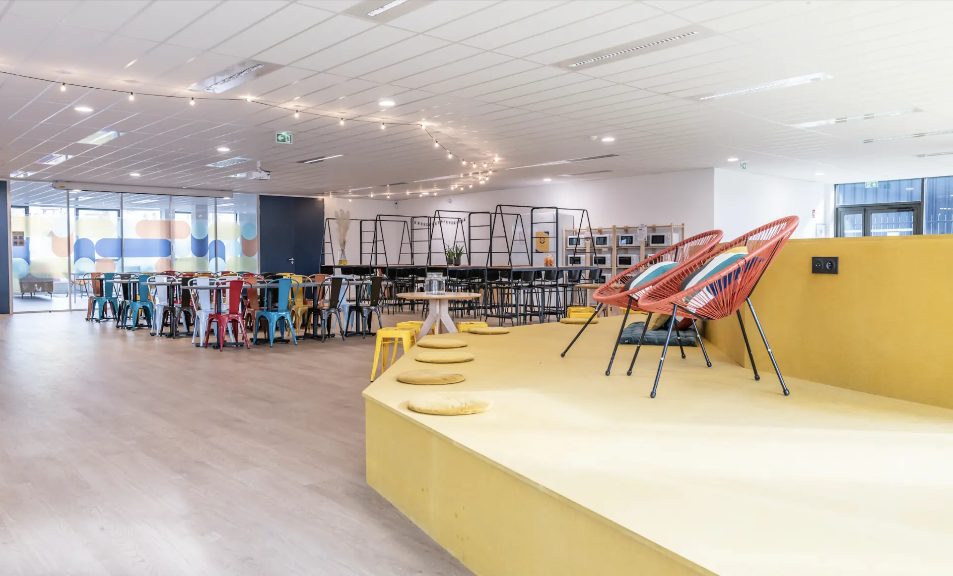 Grand espace commun du campus avec estrade, fauteuils et tables colorées
