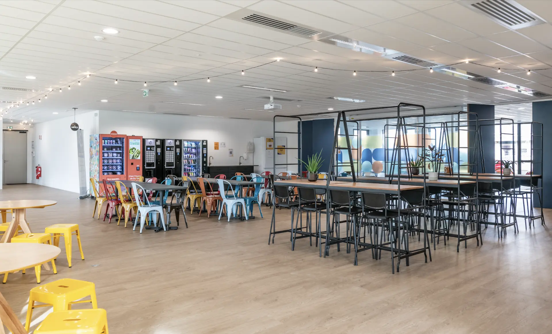 Espace de vie du campus avec tables hautes, distributeurs et coin détente